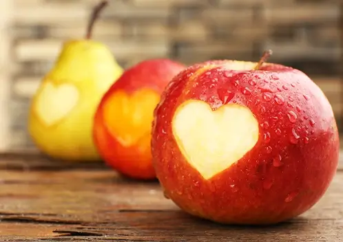 A pear and two apples with heart shaped cut outs.